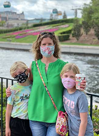 Agent Darcy and her two kids posing in Epcot with the Skyliner and France Pavilion in the background